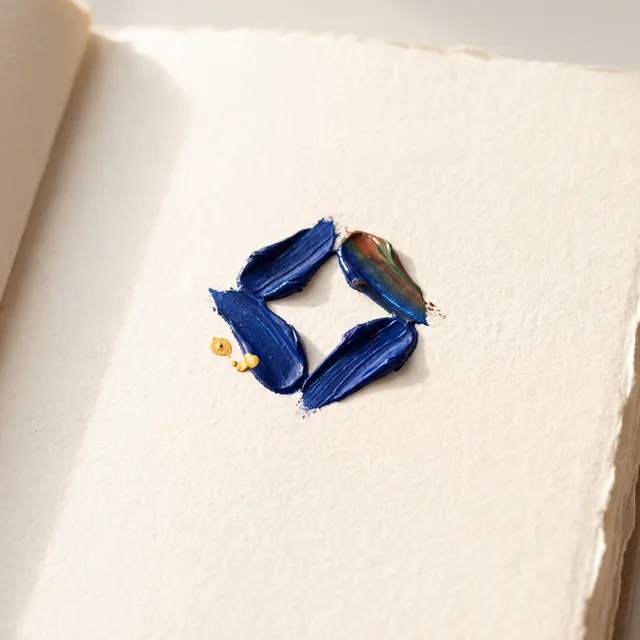 Four thick paint strokes in blue and iridescent shades form a diamond shape on textured off-white paper, accented by two small gold drops.
