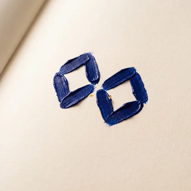Two diamond shapes rendered in thick, textured blue paint with small gold leaf accents on off-white paper.
